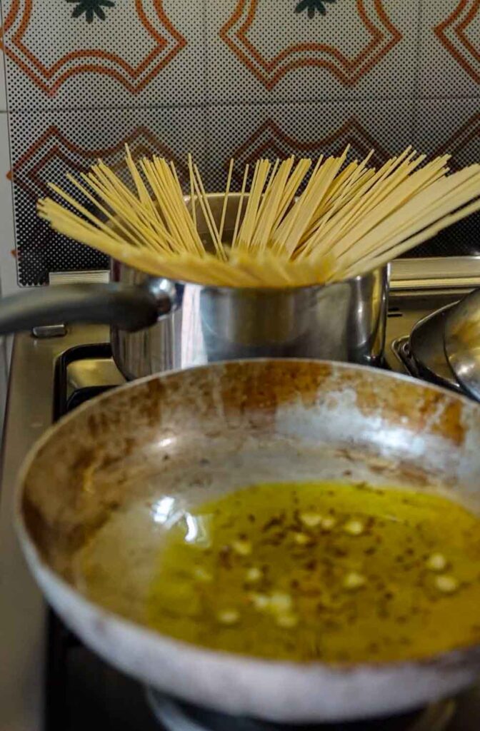 adding pasta to pasta water while oil continues to infuse